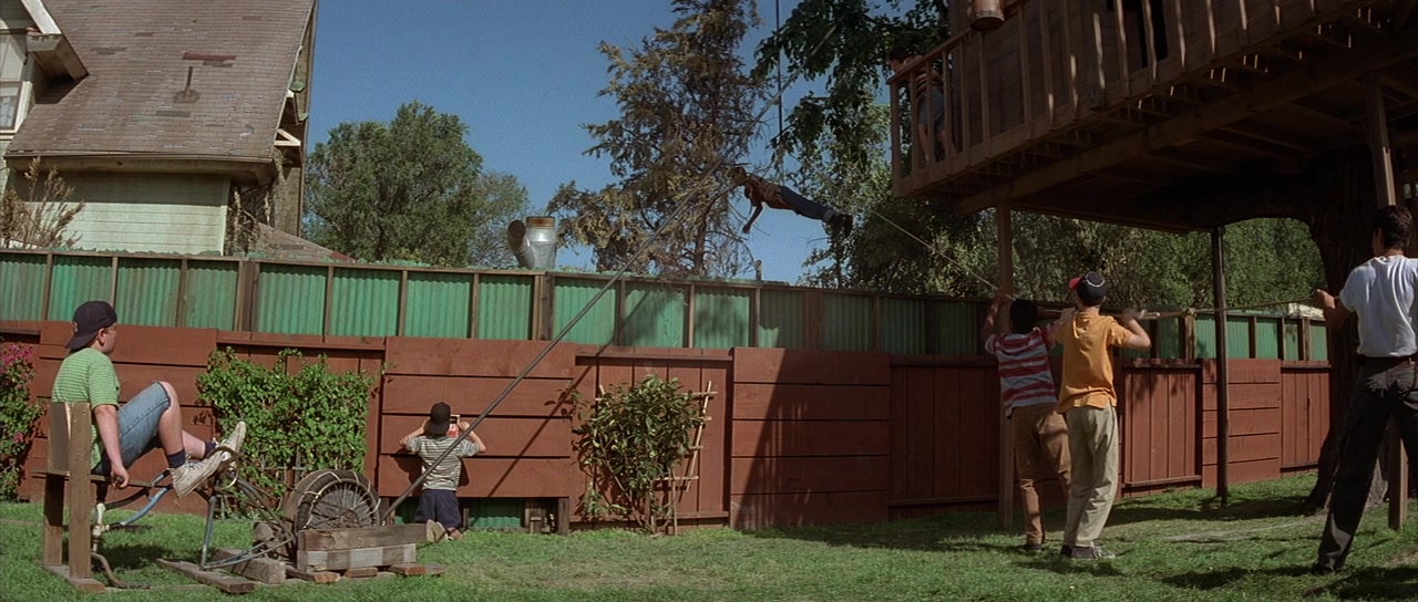 Frame from "The Sandlot" featuring a group of kids hoisting their friend over a fence via an elaborate system of pulleys.